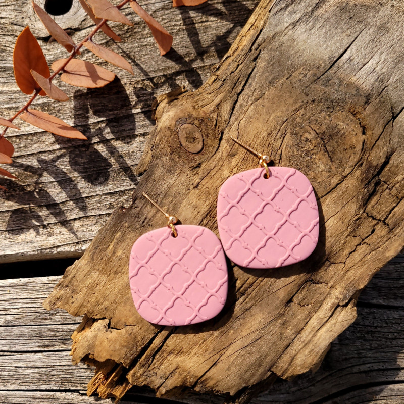 Boucles d'oreilles rose en argile avec motif délicat.